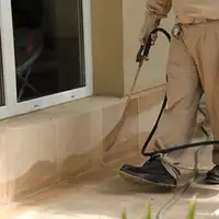 General pest control technician spraying exterior perimeter around a home in Rochester, NY