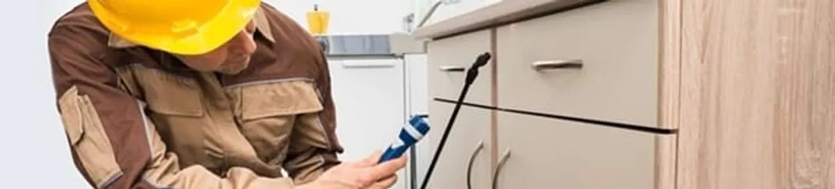 Roach exterminator applying treatment under kitchen cabinets in Rochester, NY