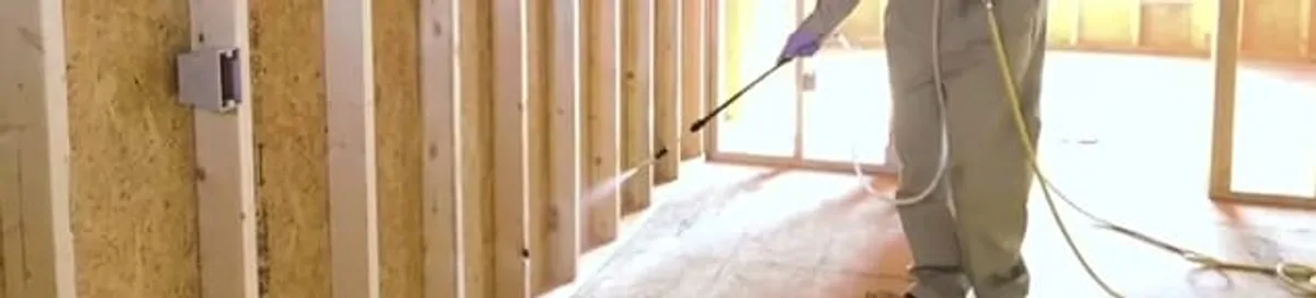 Termite treatment technician applying spray along framing and unfinished walls in Rochester, NY