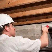 Termite inspection technician checking a basement wall and framing for termite activity in Rochester, NY